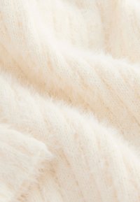 Tissu tricoté de couleur crème avec une texture douce et duveteuse et un motif côtelé, présentant des fils légers et aérés ainsi qu'un léger éclat.