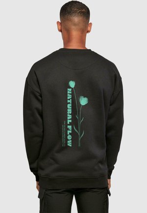 Czarny sweatshirt z zieloną grafiką kwiatową oraz napisem "NATURAL FLOW" na plecach. Materiał wydaje się miękki, a krój jest klasyczny.