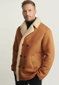 Brązowy dwurzędowy płaszcz wykonany z miękkiego materiału, z kremowym futrzanym kołnierzem, dwoma guzikami i boczną kieszenią. Gładka tekstura na całej powierzchni.