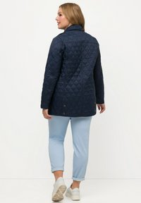 Námořnická prošívaná bunda s výstřihovým límcem, s diamantovým vzorem a knoflíkovými detaily. V kombinaci se světle modrými ohrnutými kalhotami a bílými teniskami.