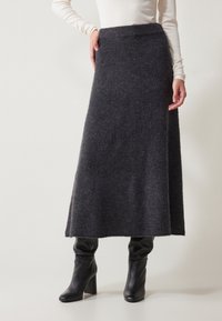 Falda de punto gris oscuro de longitud media con una cintura alta, que presenta una textura suave y elegante. Combinada con botas de tacón negras.