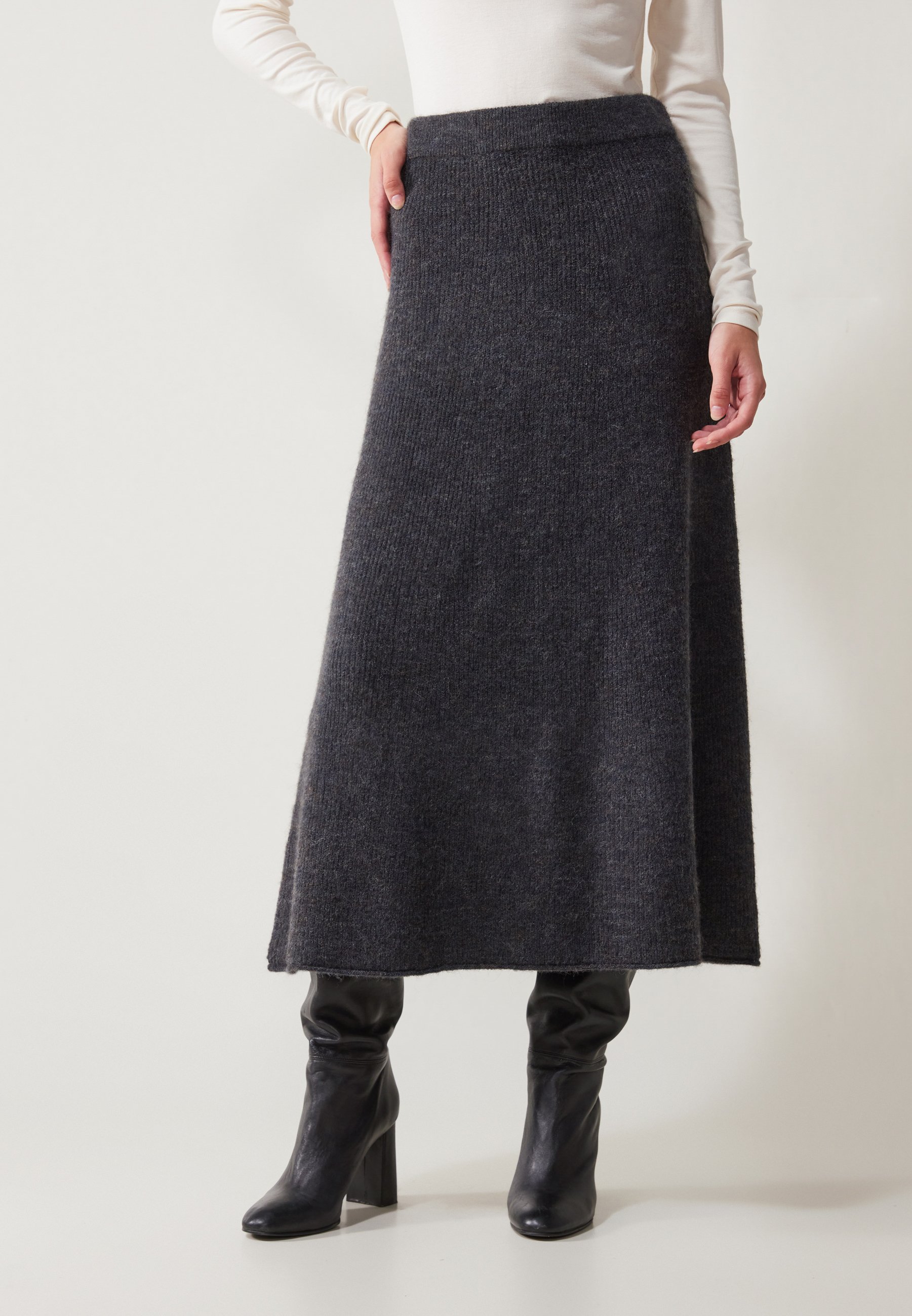 Dark gray knitted mid-length skirt with a high waistband, featuring a sleek and smooth texture. Paired with black heeled boots.