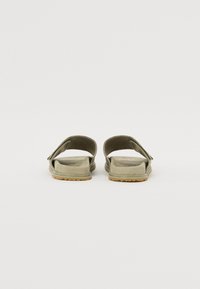 Sandales à glissière vert olive avec un dessus texturé, un design à double bride et une semelle plate dotée d'une semelle extérieure en caoutchouc marron clair.