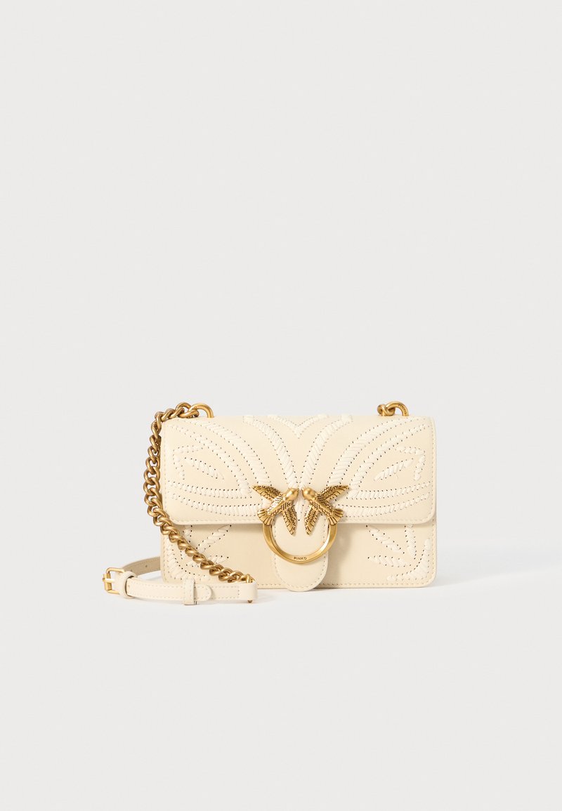 Bolsa de pele creme com acabamentos em tom de dourado, design intricado em recortes, alça de corrente e fecho circular com acentos decorativos.