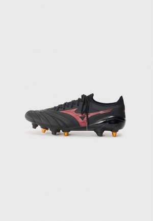 Black football cleat with textured synthetic upper, red accent design, black sole, and orange studs for traction on grass surfaces.
