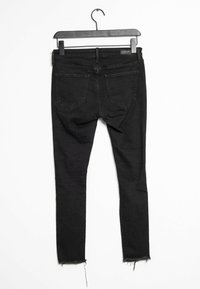 Černé skinny džíny s třepeným lemem, vyrobené z denimu, s dvěma zadními kapsami a standardním pasem. Visí na černém ramínku.