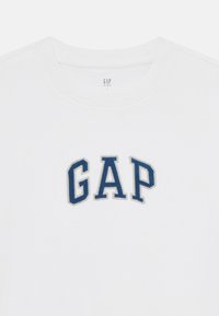 Hvit bomulls t-skjorte med en blå brodert "GAP"-logo. Klassisk crew neck-design med en myk tekstur og lett følelse.