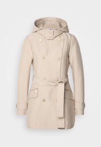 Trench-coat beige croisé avec capuche, taille ceinturée, poignets boutonnés et poches latérales zippées sur fond uni.