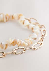 Gold chain necklace with irregular beige and white shell beads, featuring interconnected oval links and a smooth texture.