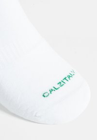Calzino bianco alla caviglia con texture a coste e logo verde "CALITALY" sulla punta. Materiale morbido ed elastico, progettato per comfort e vestibilità.