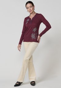 Burgundijas garām piedurknēm krekls ar izšūtām ziedu dizainiem un pogu akcentiem. Saskaņots ar krēmkrāsas platām biksēm un melniem smailiem apaviem.