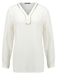 Blouse blanche à manches longues avec col en V et bordure dorée décorative autour du col, confectionnée en tissu léger.