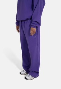 Lilla oversized hettegenser og matchende joggebukser laget av mykt stoff. Har elastisk midje og en logo på buksene. Sølvfargede joggesko.