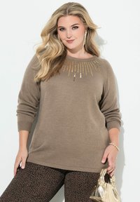 Brązowy sweter z dzianiny z ozdobami z złotych cekinów przy dekolcie, z długimi rękawami, w połączeniu z legginsami w czarno-brązowy wzór i złotą torbą.