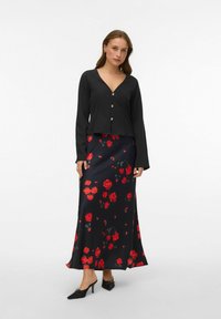 Mustast nööpidega särk koos pika musta satiinse seelikuga, millel on punane lillemuster, sile tekstuur ja küljetud. Mustad kingad täiendavad riietust.