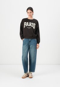 Black sweatshirt with white "PARIS" lettering, paired with wide-leg blue denim jeans and patterned beige sneakers. Simple design and relaxed fit.