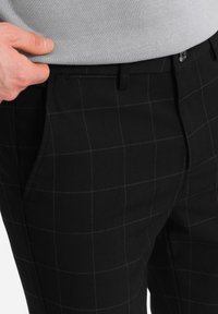 Pantalons à carreaux noirs en tissu texturé. Présentent une coupe slim et des poches latérales, avec des coutures contrastées mettant en valeur le motif en grille.