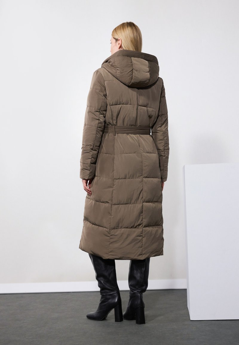 Manteau rembourré brun avec capuche, design matelassé, taille ceinturée et manches longues, associé à des bottes noires montantes. Texture lisse.