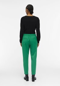 Un haut noir à manches longues associé à un pantalon vert avec une taille élastiquée, deux poches arrière, et des bottes noires à talons de hauteur cheville.