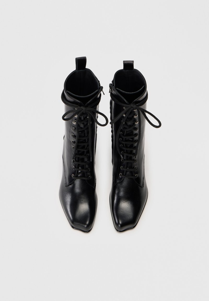 Zwarte leren enkelboots met spitse neuzen, vetersluiting aan de voorkant en een zijrits. Glad oppervlak met minimale hardware en ontwerpelementen.