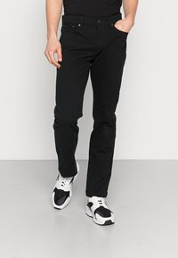 Pantaloni in denim nero con una vestibilità slim, design a cinque tasche e chiusura con bottone. Abbinati a sneakers sportive bianche e nere.