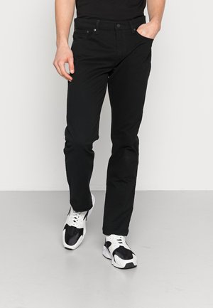 Pantalon en denim noir avec une coupe slim, design à cinq poches et fermeture à bouton. Associé à des baskets sportives blanches et noires.