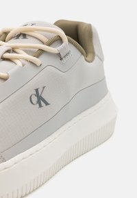 Sneakers Calvin Klein in materiale texture grigio chiaro con suola bianca, lacci beige e logo CK di lato. Forma arrotondata con collare imbottito.