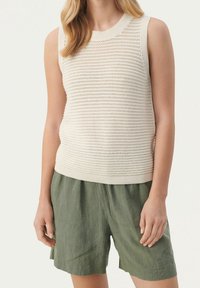 Kremowy, dziany bezrękawnik z teksturowanym wzorem i prążkowanym dołem, w połączeniu z luźnymi oliwkowymi szortami z lnu.