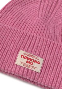 Rosa gerippte Strickmütze mit einem angenähten beigen Etikett, auf dem "THINKING MU" steht, und zusätzlichem kleinerem roten Text am Bündchen.
