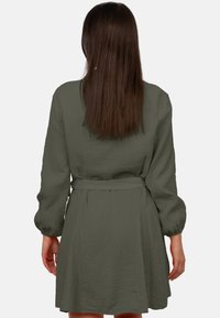 Abito verde intrecciato con maniche lunghe, cintura in vita, vestibilità rilassata, tessuto testurizzato e gonna leggermente svasata. La vista posteriore mostra una silhouette liscia.