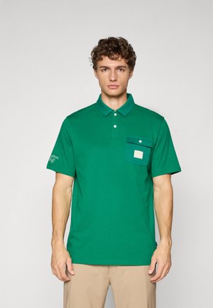 Polo vert en coton, avec une poche à boutons et un logo sur la manche. Manches courtes et design de col classique.