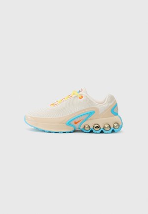 Creme- und hellblauer Sportschuh mit gelben Schnürsenkeln, orangefarbenem Nike-Swoosh und abgerundeten Polsterelementen an der Seite der Sohle.