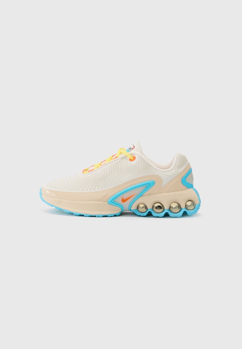 Chaussure de sport crème et bleu clair avec des lacets jaunes, un logo Nike orange et des éléments de coussin arrondis sur le côté de la semelle.