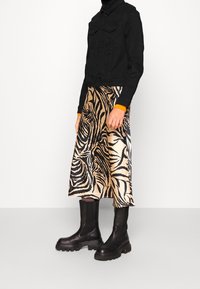 Svart denimjacka, midi kjol i beige och svart med djurtryck i satin, och kraftiga svarta stövletter med strukturerade suler.