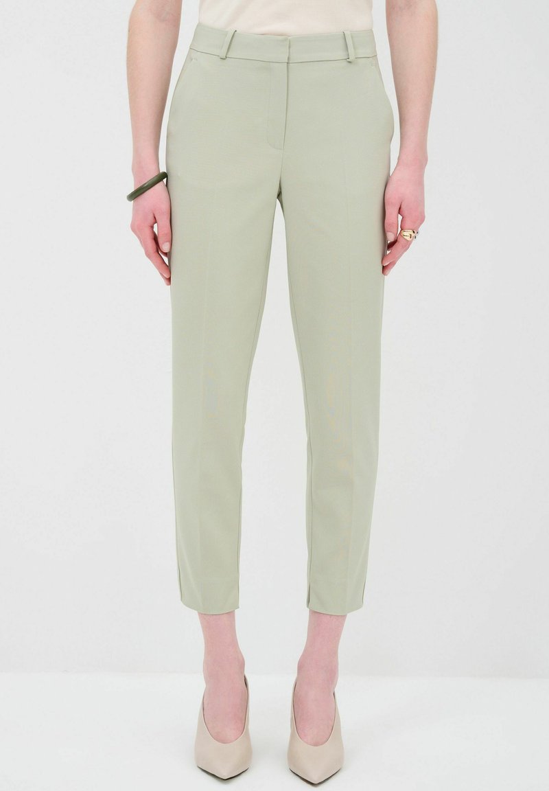 Světlé zelené kalhoty na míru se slim fit, s předními kapsami, poutky na opasek a zkráceným lemem, kombinované s nahými lodičkami na vysokém podpatku.