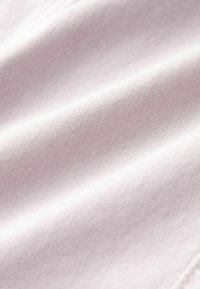 Tissu rose pâle à texture lisse, présentant un tissage fin. La surface montre de doux plis et un léger éclat sous la lumière naturelle.