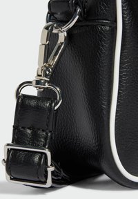 Black leather handbag with textured finish, featuring a silver metal clip and buckle strap, accented by a white piped edge.