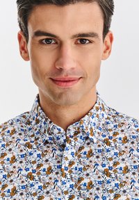 Biała koszula w kwiatowy wzór w odcieniach niebieskiego, brązowego i pomarańczowego; posiada kołnierzyk zapinany na guziki oraz subtelną fakturę.