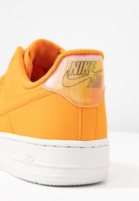 Talons de basket Nike Air orange avec semelle blanche et logo "NIKE AIR" sur un fond dégradé sur l'étiquette du talon.