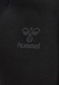 Zwart atletisch materiaal met een subtiele logodesign met een bijmotief en de merknaam "hummel" in een ton-sur-ton afwerking.