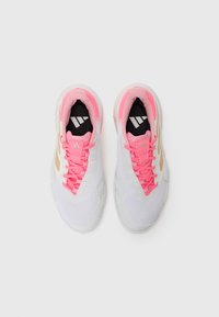 Zapatillas deportivas blancas con cordones y acentos rosas, collar acolchado, parte superior de malla y suela texturizada con un patrón geométrico. Plantilla negra con logo.