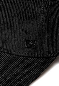 Černá kordurová čepice s jemně vroubkovanou texturou, zakřiveným špicem a vyšitým logem "BS" ve tkanině. Detailní pohled.