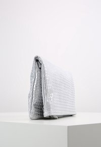 Stříbrná kabelka na ruku s krokodýlí texturou, hladký syntetický materiál, obdélníkový tvar a skládací design. Minimalistický a elegantní vzhled.