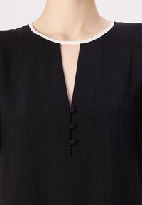 Black dress featuring a textured fabric with a subtle striped pattern, a keyhole neckline, and three round button accents down the front.