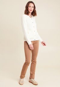 Cardigan in maglia crema con tessuto testurizzato e bottoni in legno, abbinato a pantaloni aderenti beige chiaro e sneakers beige.