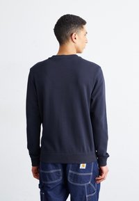 Felpa blu navy con maniche lunghe, scollo rotondo e polsini a coste. Texture liscia, design semplice e minimalismo nei dettagli sul retro.