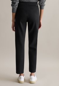 Schwarze, maßgeschneiderte Hose mit glatter Textur und figurbetonter Silhouette, ausgestattet mit einem mittelhohen Bund und leichter Verjüngung zum Knöchel hin.