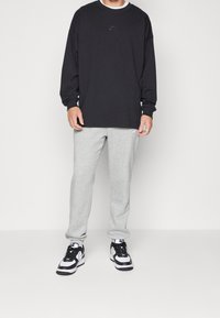 Svart långärmad t-shirt med en liten grå Nike-logotyp, kombinerad med grå mjukisbyxor och svart-vita sneakers.