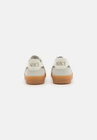 Os sapatilhas Nike apresentam um cabedal de couro branco com detalhes em verde, uma sola de borracha de goma e um logótipo estampado no calcanhar.