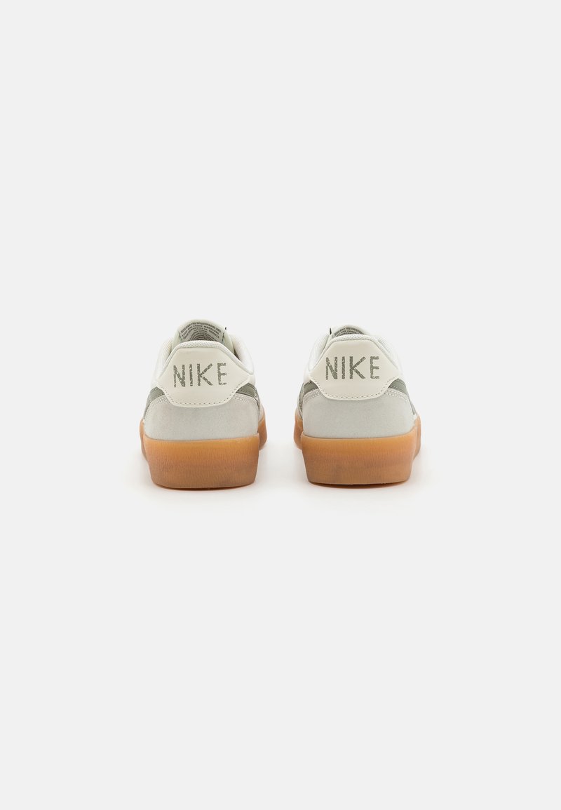 Las zapatillas Nike cuentan con una parte superior de cuero blanco con detalles en verde, una suela de goma, y un logo en relieve en el talón.